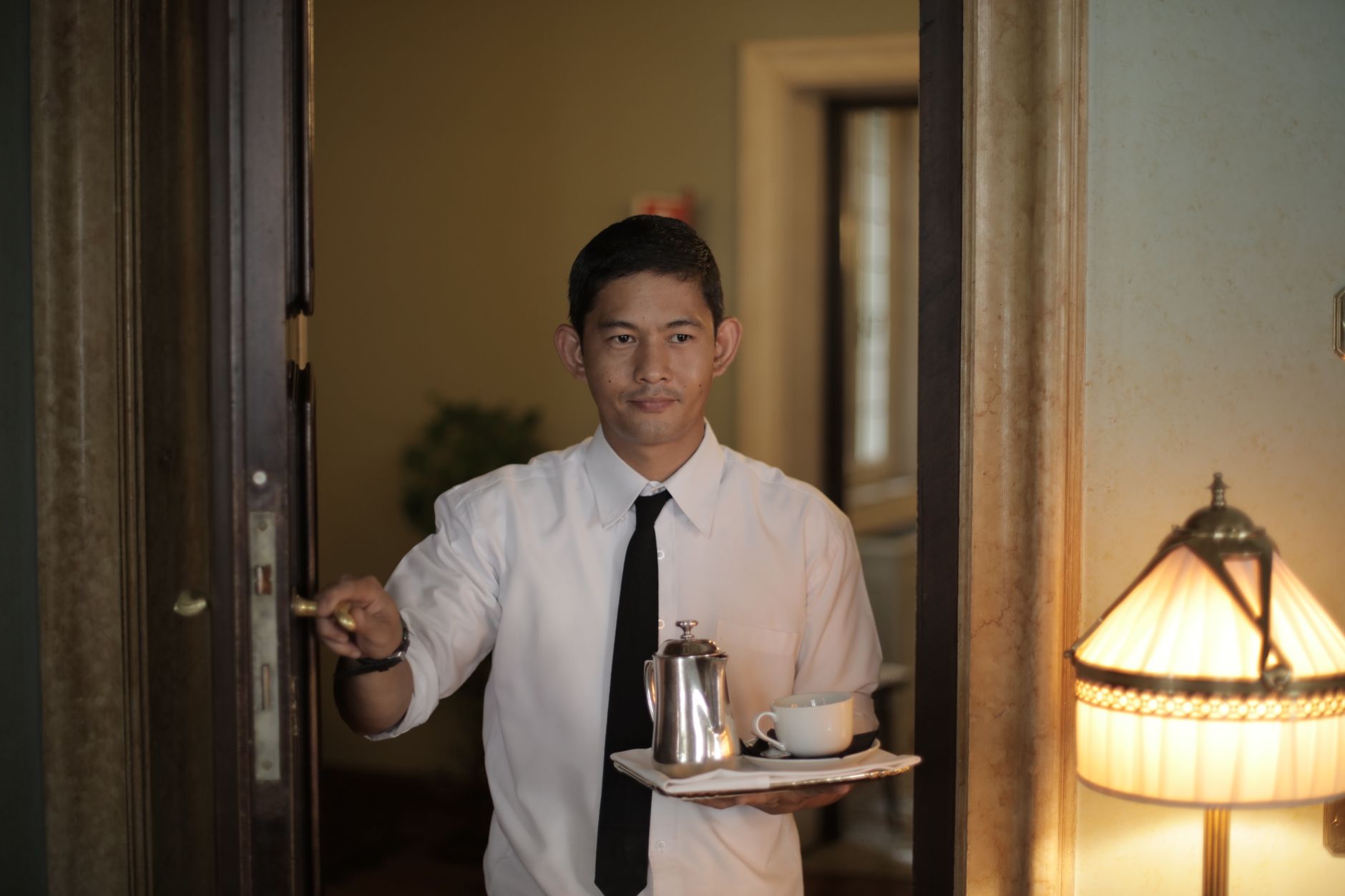 Positive ethnic male employee carrying tray with coffee while serving guest in cozy hotel room. Photo by Andrea Piacquadio on Pexels