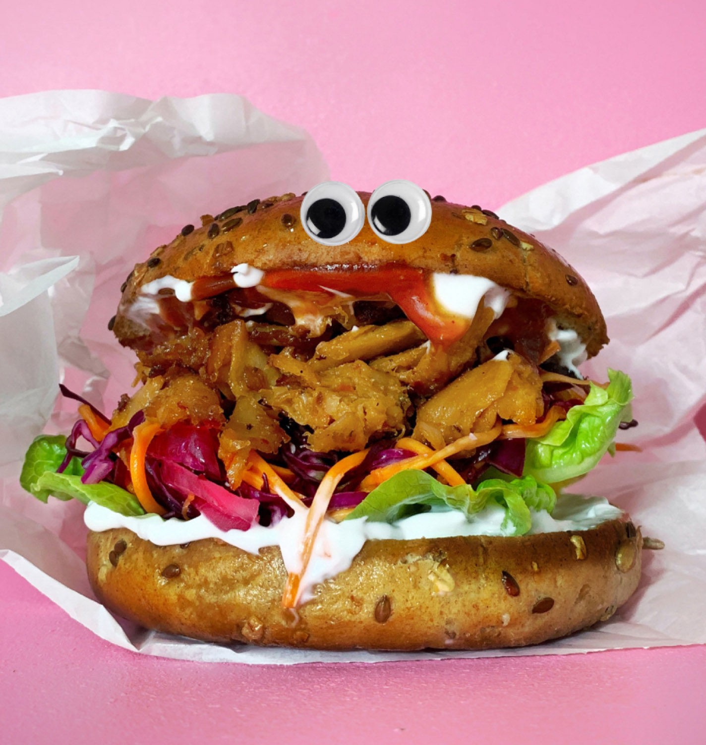 Burger with googly eyes and mayonnaise in paper wrapping on pink background