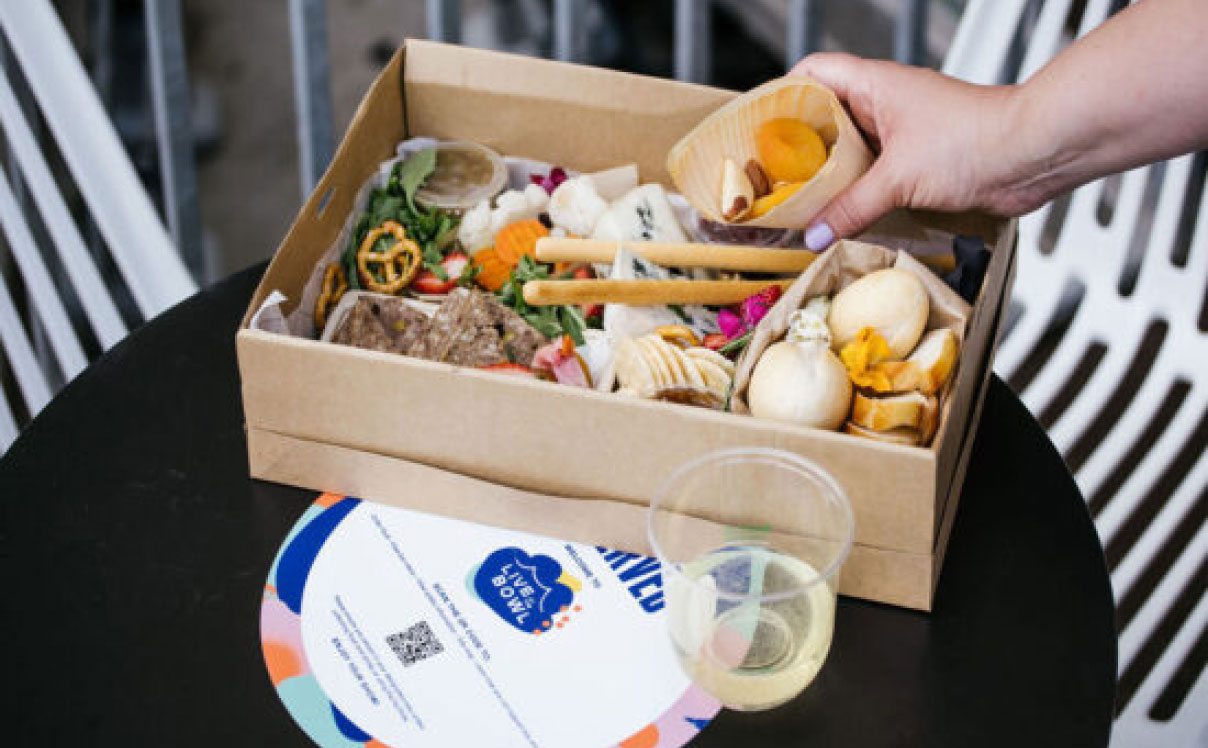 Person holding food from grazing box with Live at the Bowl x HungryHungry QR Code Sticker