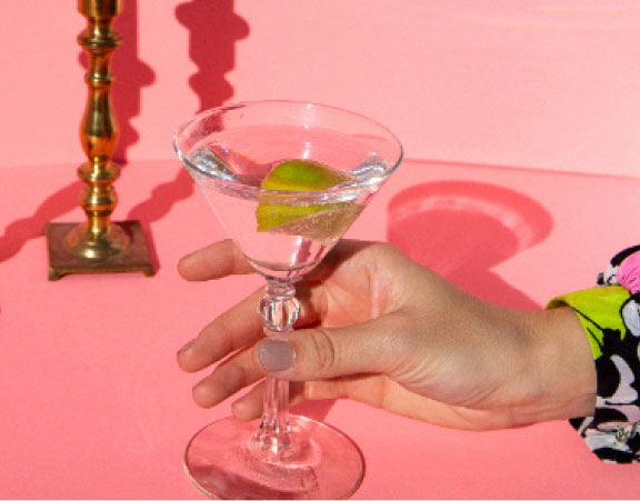 Female hand grabbing martini glass on pink background with shadows