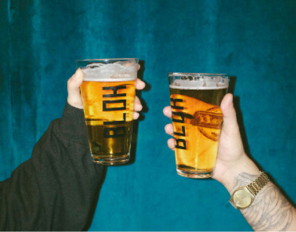 Two hands holding glasses of beer side by side on blue curtain background