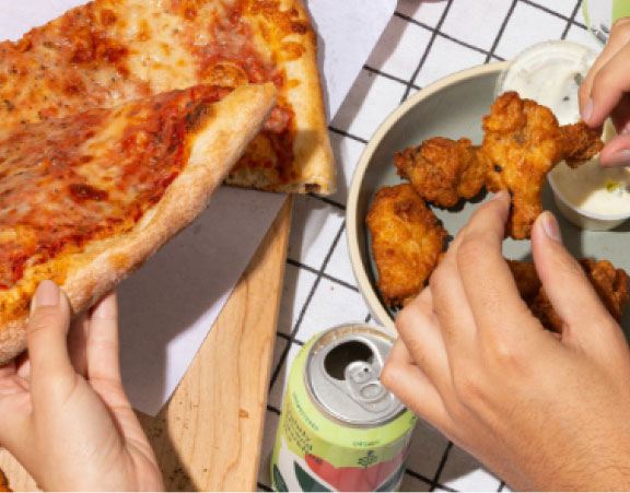 Pizza and chicken wing food image close up being shared by two people