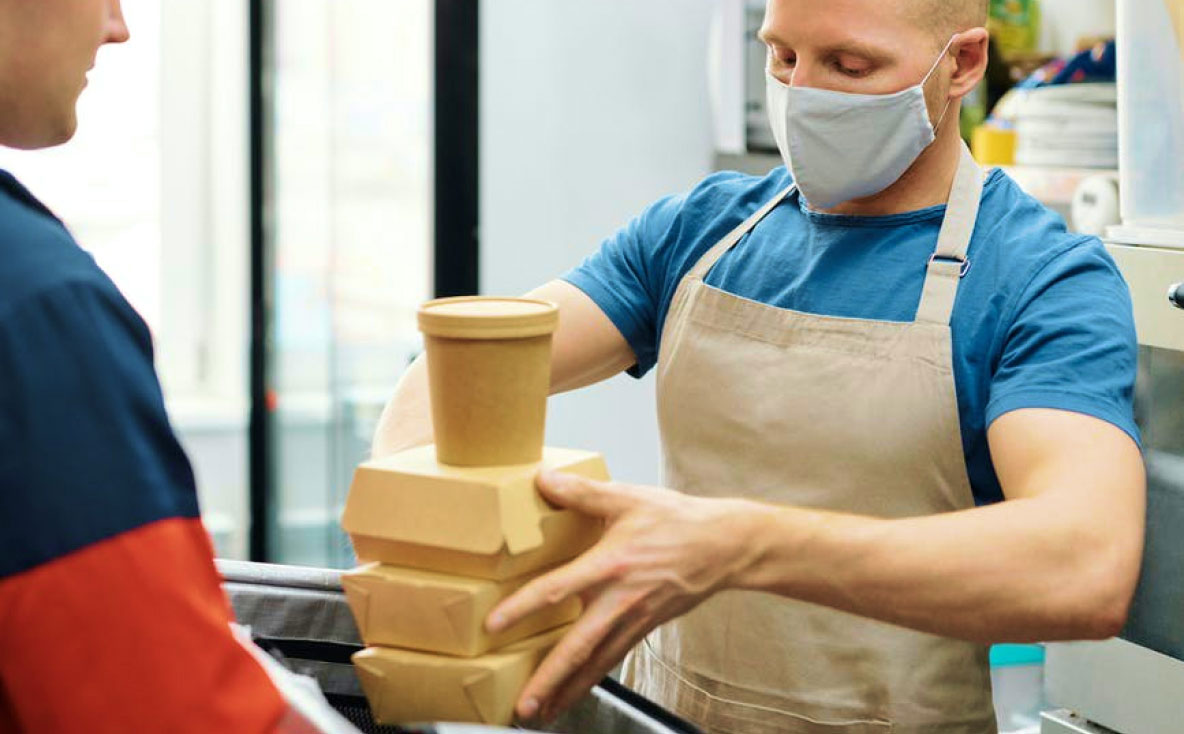 Man with mask giving food takeaway boxes to a delivery man to take to a customer