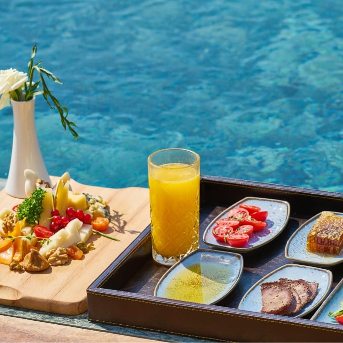 Breakfast platter with various ingredients such as fruit and tomatoes with a glass of orange juice by the pool