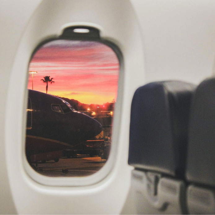 View through airplane window looking onto more planes in a pink sunset